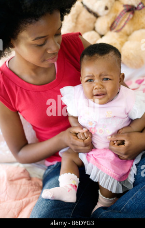 Teenage mother and baby. Four month old baby girl crying on her mother's knee. Posed by models. Stock Photo