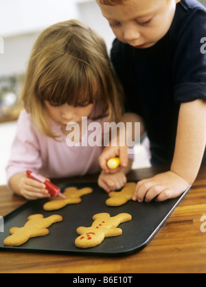 Making biscuits. Two three year old children decorating freshly baked biscuits with coloured icing. Stock Photo