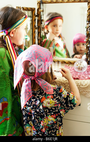 Dressing up. Four year old girl using a mirror to apply lipstick during a dressing up game. Stock Photo