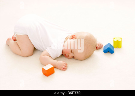 Baby girl (6-11 months) sleeping on the floor surrounded by toy blocks Stock Photo