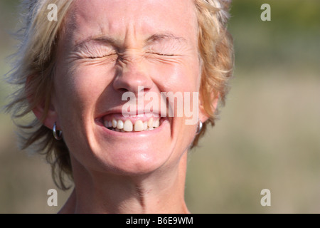 Portrait of a young blonde woman outdoors with eyes tight shut. Stock Photo