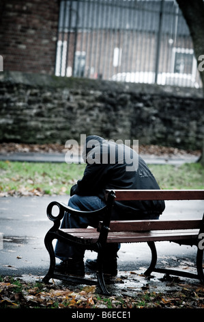 Young man wearing a hooded jacket depressed lonely alone and isolated sitting on a park bench UK Stock Photo