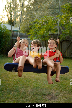Three childhood friends on swing in backyard Stock Photo