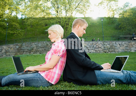 Guy and girl sitting back to back in a park Stock Photo
