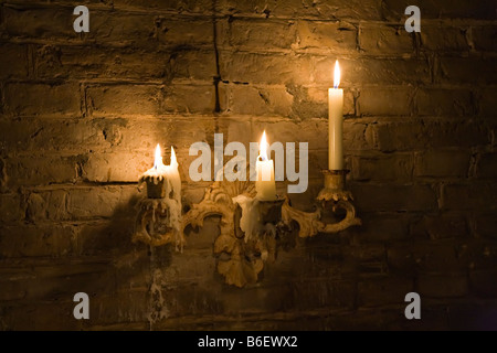 Candles burning in old candleholder fixed to wall Stock Photo