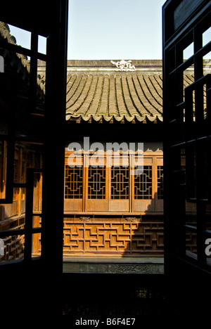 Lattice work window onto stone tile roof overlooking intricately decorated wood paneling  inner courtyard Gangzhou Assembly Hall Stock Photo
