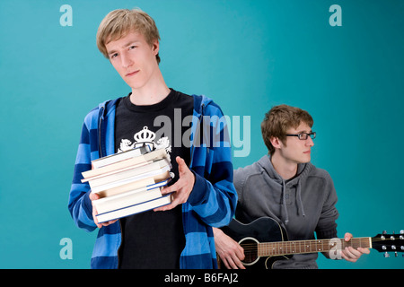 Young man holding a pile of books and another playing guitar Stock Photo