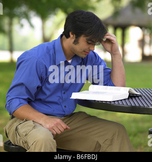 young man sitting at a table in a park, reading a book Stock Photo