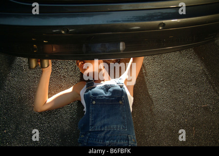 Young woman in working clothes is lying under her car while fixing it Stock Photo