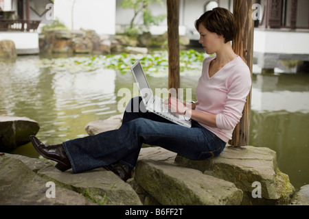 Young woman, student working on a laptop in a Chinese garden Stock Photo