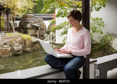 Young woman, student working on a laptop in a Chinese garden Stock Photo
