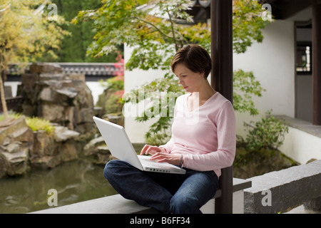 Young woman, student working on a laptop in a Chinese garden Stock Photo