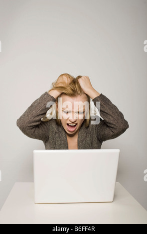 Young long-haired woman yelling in despair at her computer, notebook, tearing her hair Stock Photo