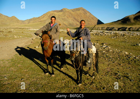 Nomads, two young men wearing traditional costumes with rifles sitting on their horses in the steppe, Kharkhiraa, Mongolian Alt Stock Photo