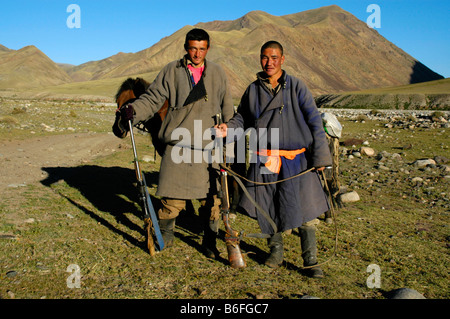 Nomads, two young men wearing traditional costumes with rifles standing in the steppe, Kharkhiraa, Mongolian Altai near Ulaango Stock Photo