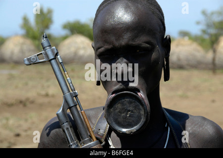 Woman with plate lip and a machine gun, Kalashnikov, from the Mursi tribe, Jinka, Ethiopia, Africa Stock Photo