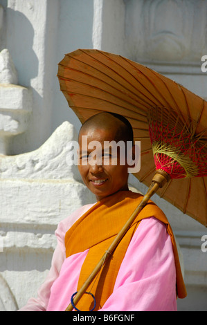 Smiling Buddhist nun wearing a pink robe and holding a paper sun umbrella, Mingun, Burma, Southeast Asia Stock Photo