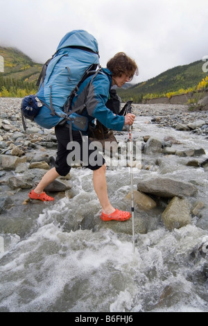 Young woman, backpacker, hiker wading through a creek, St. Elias Mountains, Donjek Route, Kluane National Park, Yukon Territory Stock Photo