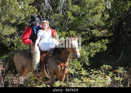 A young lady and cowboy riding horseback in the woods Stock Photo
