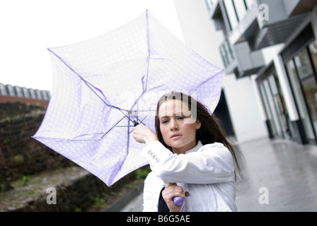 Attractive young woman struggling as her umbrella is blown around in the wind on a rainy day Stock Photo