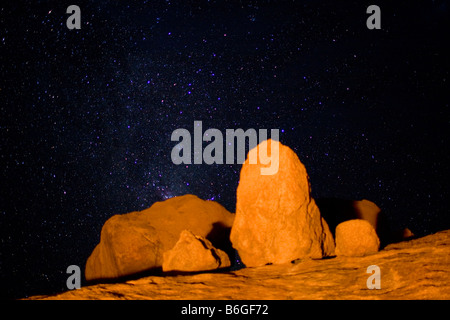 Africa Namibia Usakos Orange light from campfire illuminates granite boulders near Spitzkoppe mountain below starry night sky Stock Photo