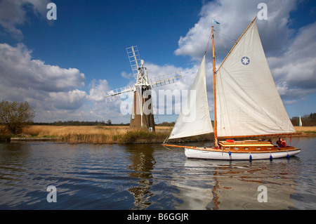 A traditional wooden sailing boat sailing in front of Turf Fen windmill on the River Ant Norfolk Broads Stock Photo
