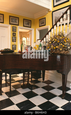 Dried flower arrangement on grand piano in yellow country hall with black and white chequerboard vinyl flooring Stock Photo