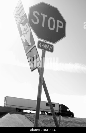Two road signs with a semi-truck driving down the highway in the background