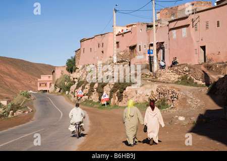 Typical Berber mountain village scene with two traditionally dressed women walking beside road. Tahanaoute Asni Valley Morocco Stock Photo