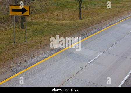 A yellow turn sign on the side of the freeway approaching a sharp turn Stock Photo