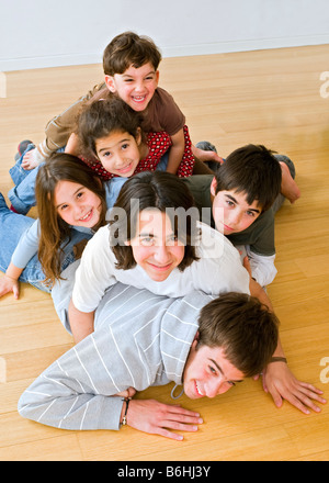 six kids in different ages piled on each other on the floor Stock Photo