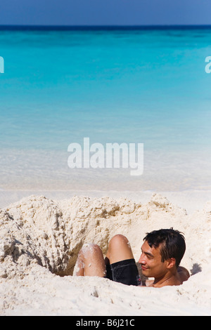 A young man in sitting in a shallow hole on a beach in The Maldives Stock Photo