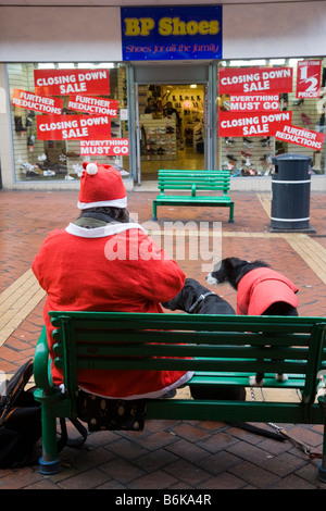 Seated homeless Tramp wearing Father Christmas outfit in Derby High Street, with dog selling Big Issue, UK Stock Photo