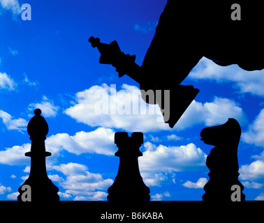 male hand moving chess pieces silhouetted on chess board with clouds background Stock Photo