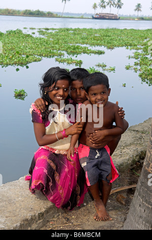 Three young children on banks of canal in backwaters of Kerala India Stock Photo