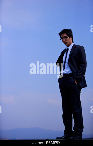 Young businessman with hands in pockets against blue sky Stock Photo