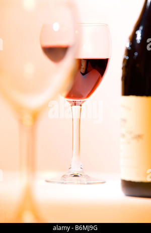 A wine glass in focus viewed through another glass near a bottle of red wine Stock Photo