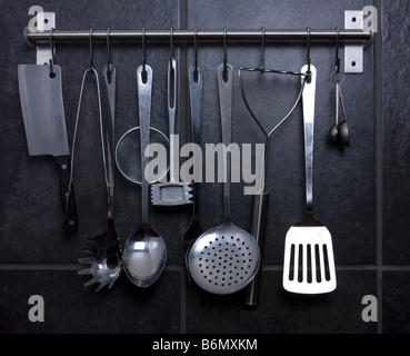various stainless steel kitchen utensils hanging from ikea rail against black slate effect tiles