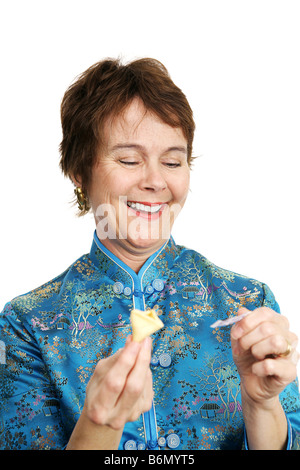 A pretty mature woman dressed in a silk chinese blouse opening a fortune cookie and laughing at the fortune inside Stock Photo