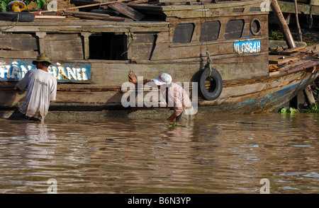 Man inspecting the hull of a boat in the Mekong Delta region of Vietnam ...