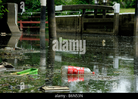 River pollution: plastic bottles, tubs, wood and deadfall floating on surface of River Wey with lock gates behind, Surrey Stock Photo