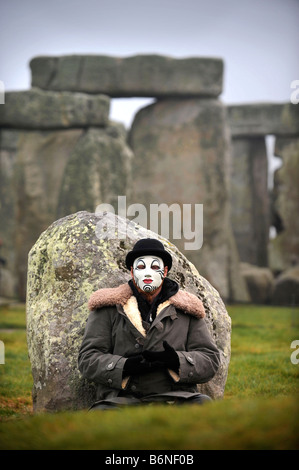 A VISITOR TO STONEHENGE WEARING A WHITEFACE CLOWN MASK SITS BY AN OUTER STATION STONE DURING THE CELEBRATIONS OF THE WINTER SOLS Stock Photo
