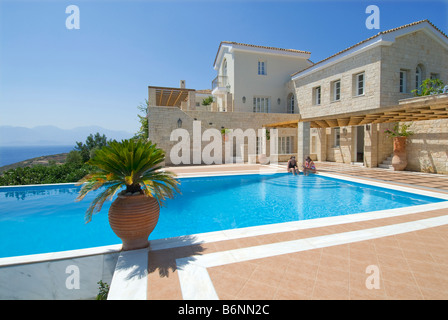 Luxury holiday vacation villa and exclusive private sunny infinity pool overlooking Crete and Aegean sea with palms and typical grecian urns Stock Photo