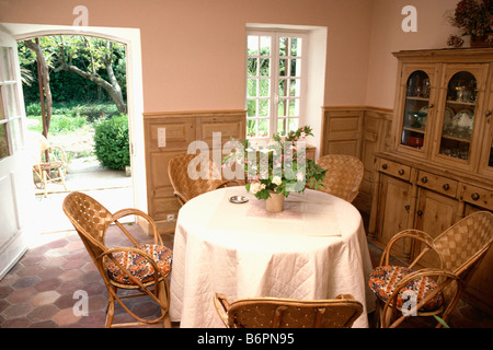 White quilted cloth on circular table with rattan chairs in peach French country dining room with open door to garden Stock Photo