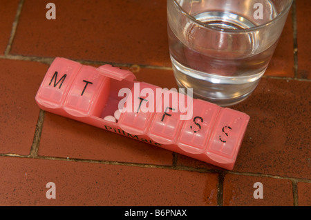 pill dispenser containing a person s medication for 7 days with a glass of water Stock Photo