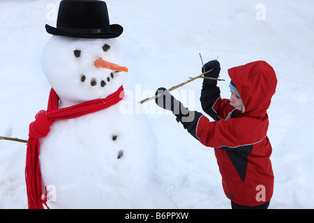 Young boy putting stick arm on snowman Stock Photo