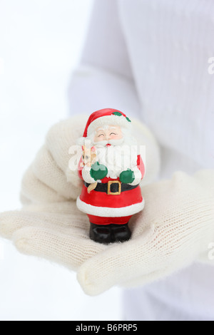 Hands with winter gloves holding Santa Claus Christmas figure Stock Photo