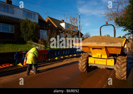 Workman using heavy duty pounder to pound gravel in road after laying electrical cabling with dumper truck parked on road Stock Photo