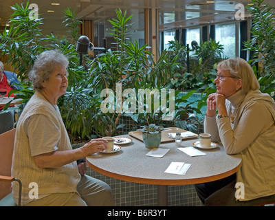 middleaged woman visiting her mother in home for old people having chat drinking coffee eating cake Stock Photo