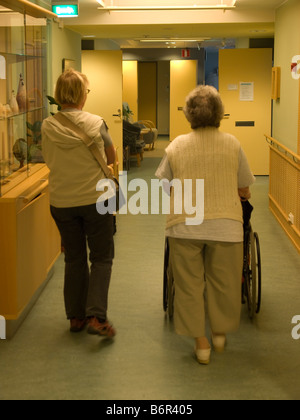 middleaged woman visiting her mother in home for old people going for a walk in corridore Stock Photo